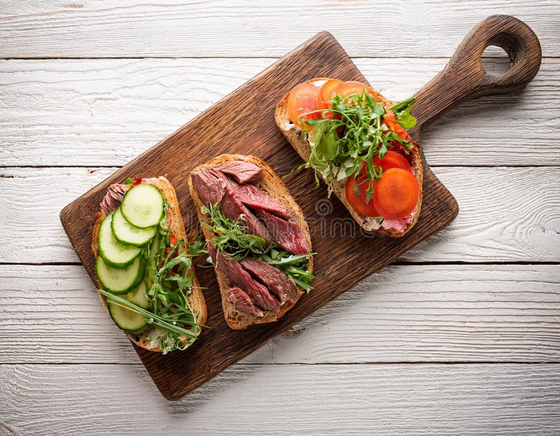 Sandwiches with beef, fresh vegetables and herbs on rustic wooden chopping board over white wood backdrop, top view. royalty free illustration