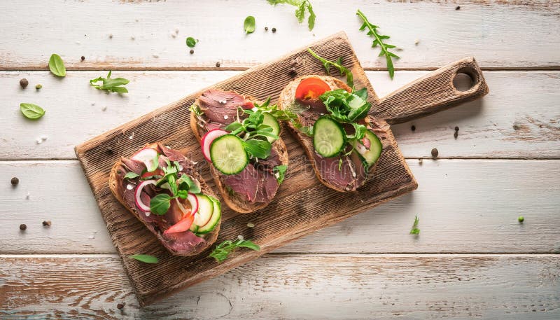 Sandwiches with beef, fresh vegetables and herbs on rustic wooden chopping board over white wood backdrop, top view. royalty free illustration