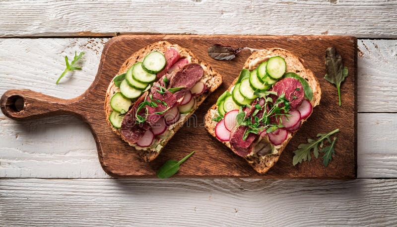 Sandwiches with beef, fresh vegetables and herbs on rustic wooden chopping board over white wood backdrop, top view. stock illustration