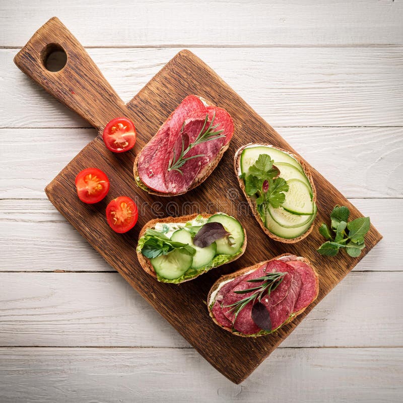 Sandwiches with beef, fresh vegetables and herbs on rustic wooden chopping board over white wood backdrop, top view. royalty free illustration