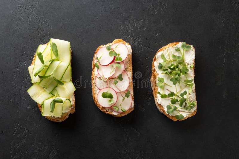 Sandwiches with sundries tomatoes, fresh radish, microgreens, cream cheese on black . Top view