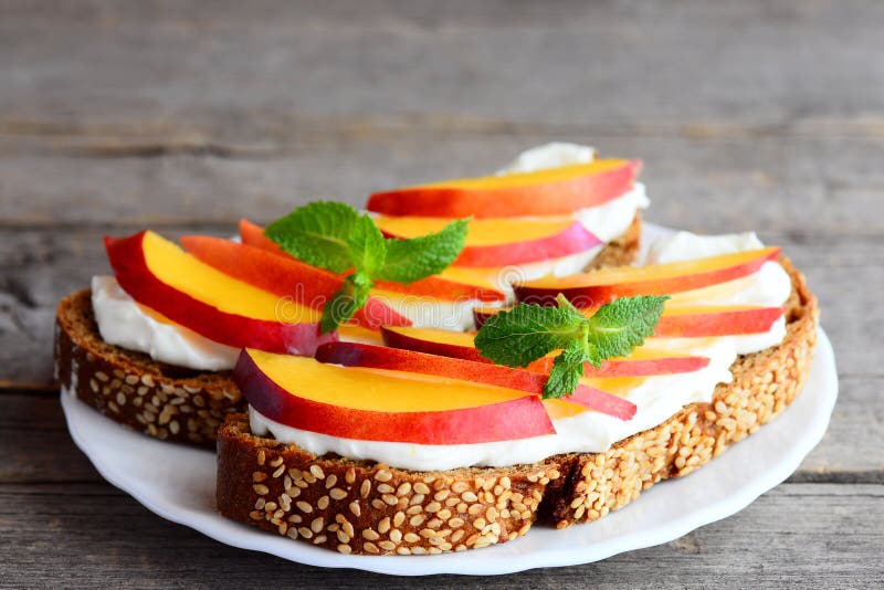 Sandwichs faciles avec le fromage fondu, les nectarines fraîches et la menthe d'un plat sur la table en bois de vintage photographie stock libre de droits Sandwichs faciles avec le fromage fondu, les nectarines fraîches et la menthe d'un plat sur la table en bois de vintage photographie stock libre de droits