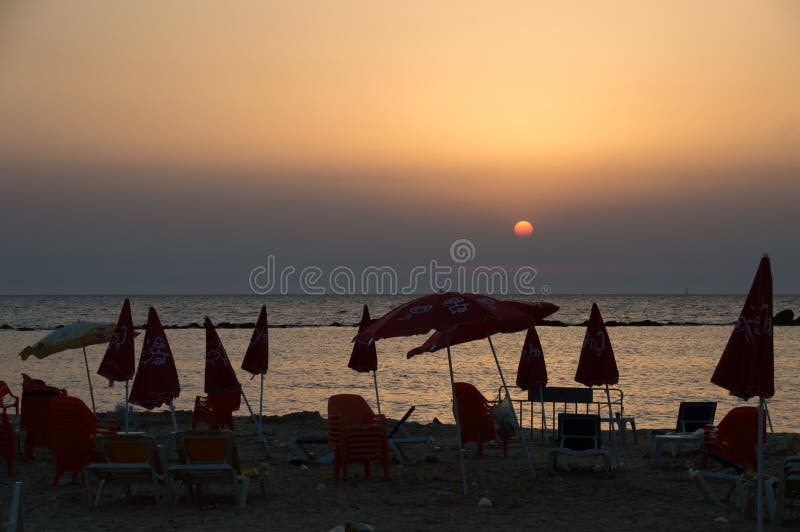 Sandy Beach sujo, enchido com os parasóis vermelhos e as cadeiras do lixo plástico no por do sol do verão fotografia de stock Sandy Beach sujo, enchido com os parasóis vermelhos e as cadeiras do lixo plástico no por do sol do verão fotografia de stock