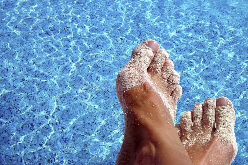 Sandy, suntanned feet with blue pool water as background. Sandy, suntanned feet with blue pool water as background