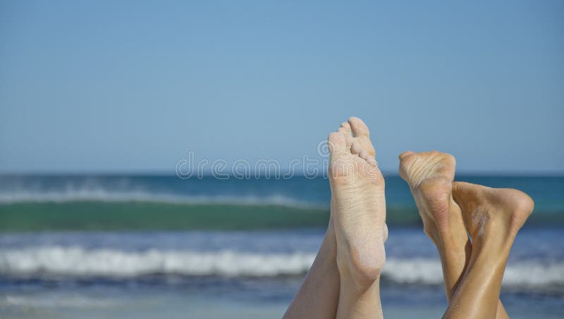 Closeup of sandy female feet at a sunny beach with copy space and blurred ocean in the background. Closeup of sandy female feet at a sunny beach with copy space and blurred ocean in the background.