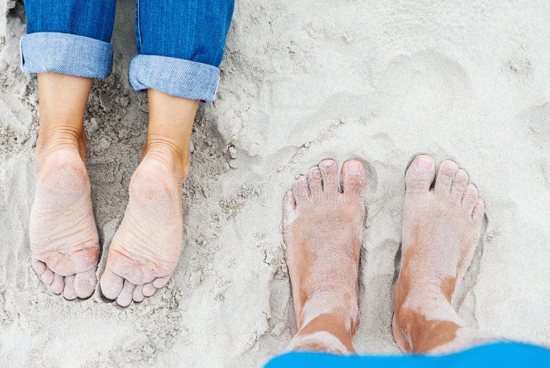 Sandy female and male feet on the beach at summer, top view