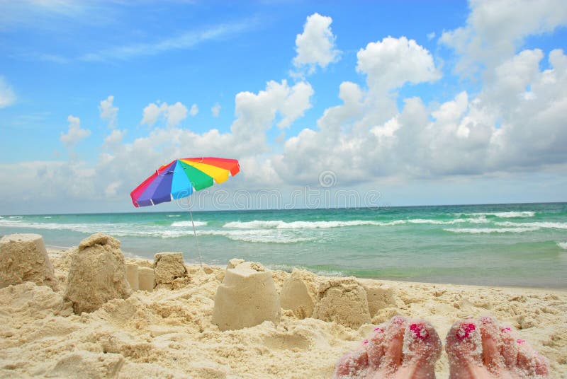 Woman's sandy toes laying next to sandcastles at pretty oceanside setting. Woman's sandy toes laying next to sandcastles at pretty oceanside setting