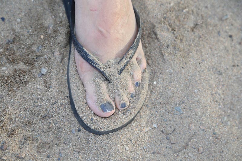 Sand shown covering the toes and foot along with flip-flop on a tropical beach. Sand shown covering the toes and foot along with flip-flop on a tropical beach