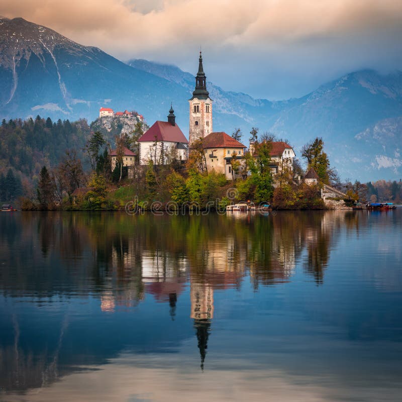 Sanguinato, la Slovenia - la bella alba di autunno nel lago ha sanguinato con la chiesa famosa di pellegrinaggio del presupposto immagini stock Sanguinato, la Slovenia - la bella alba di autunno nel lago ha sanguinato con la chiesa famosa di pellegrinaggio del presupposto immagini stock