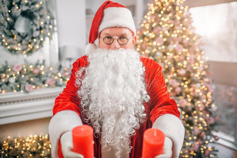 Santa Claus-de tribunes alleen in ruimte en houdt twee rode kaarsen in habds Hij toont hen op camera De mens is ernstig en stock fotografie Santa Claus-de tribunes alleen in ruimte en houdt twee rode kaarsen in habds Hij toont hen op camera De mens is ernstig en stock fotografie
