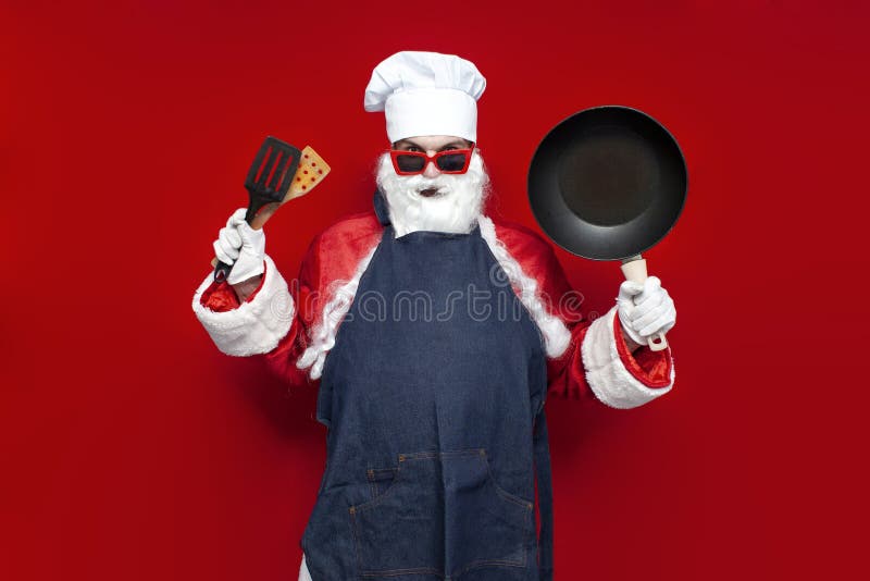 Santa claus en chefs chapeau et tablier tient poêle et ustensiles de frire sur fond rouge cuisinier mâle en costume santa photos stock