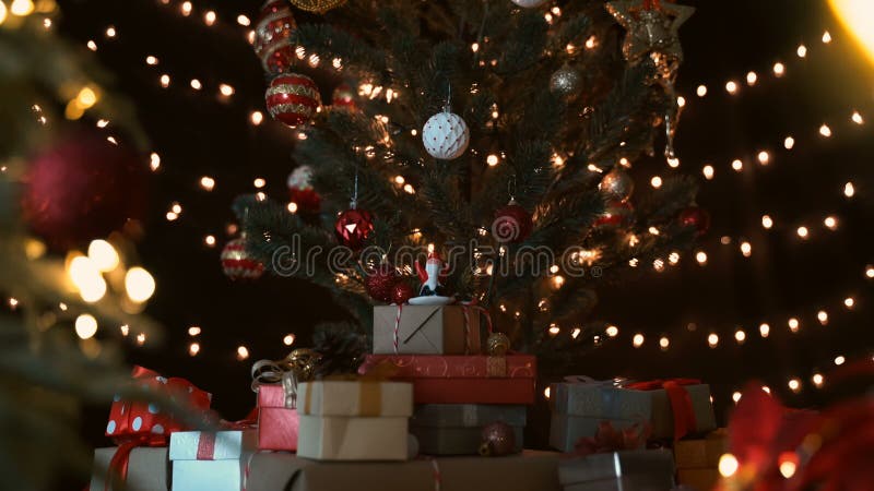 Santa claus figine met een stapel cadeaudozen onder een prachtige kerstboom tegen grote lichten ' s nachts