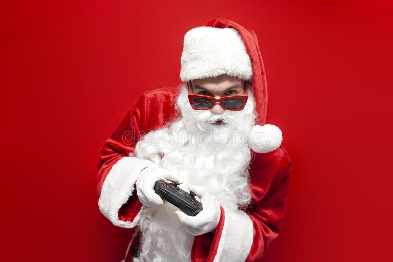 Santa claus gamer dans les lunettes festives et chapeau joue jeu vidéo sur gamepad sur fond rouge photos stock