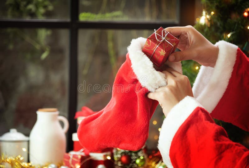 Santa claus hands are holding a Red gift or present box and Christmas stocking.