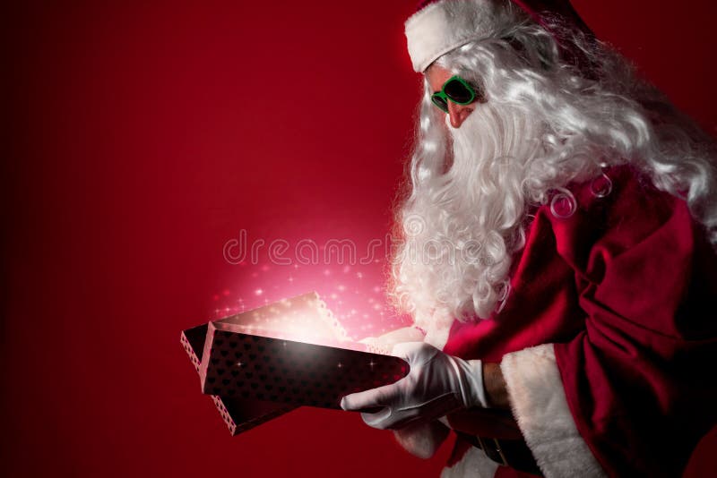 Santa Claus opening a gift box full of Christmas magic dust on a red background