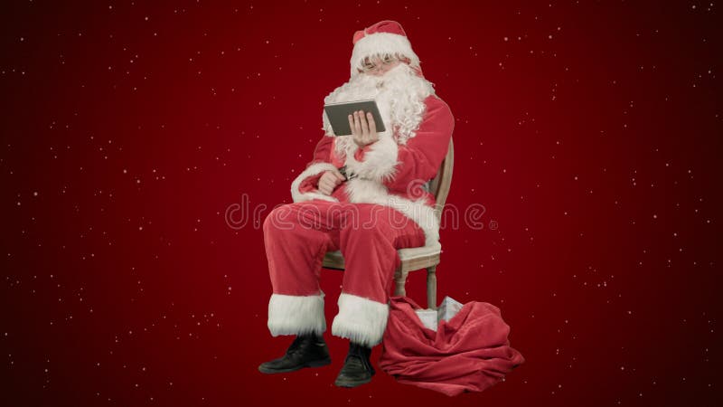 Santa Claus que usa o tablet pc para surfar o Internet e comunicar-se em meios sociais com as crianças no fundo vermelho com foto de stock royalty free Santa Claus que usa o tablet pc para surfar o Internet e comunicar-se em meios sociais com as crianças no fundo vermelho com foto de stock royalty free