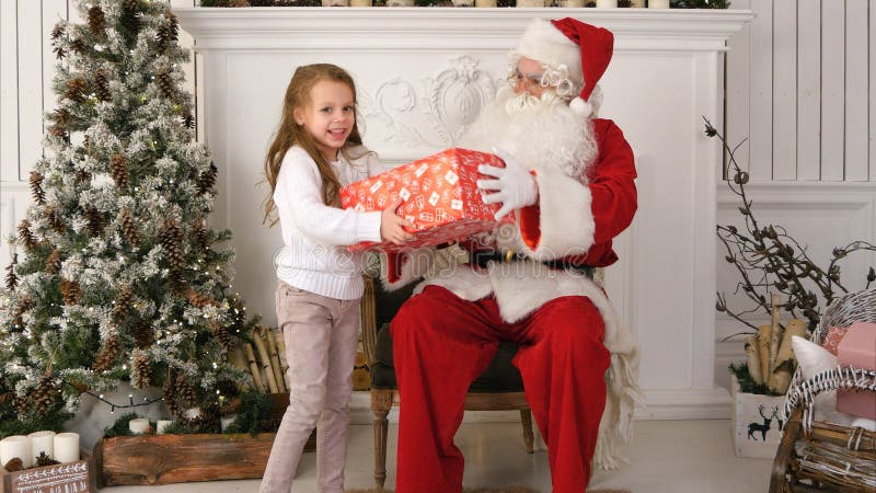 Santa Claus som ger en utmärkt slågen in gåva till en gullig liten flicka royaltyfri fotografi Santa Claus som ger en utmärkt slågen in gåva till en gullig liten flicka royaltyfri fotografi