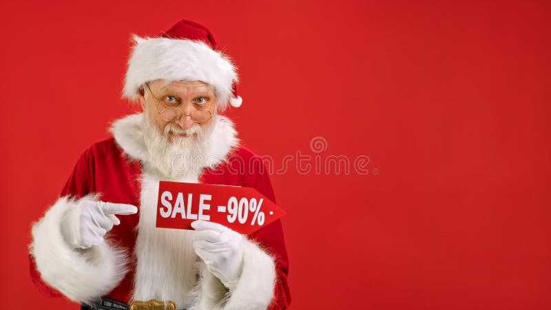 Santa Claus Holds Sign With Inscription Sale -90 off, Points His Finger at an Empty Space Mock up and Looks at Discount in Camera and Smiles on Red Background. Big Discount, Christmas Holidays Sales. Santa Claus Holds Sign With Inscription Sale -90 off, Points His Finger at an Empty Space Mock up and Looks at Discount in Camera and Smiles on Red Background. Big Discount, Christmas Holidays Sales