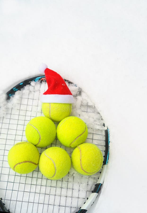 Santa hat on tennis ball, set of tennis balls in shape fir tree on racket on white snow winter background. Merry Christmas and New