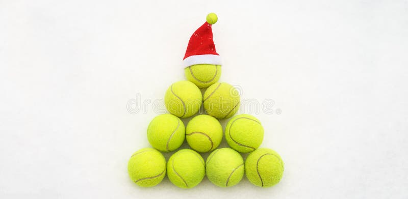 Santa hat on tennis ball on white snow background. Christmas and New year concept with tennis balls. Yellow green color tennis