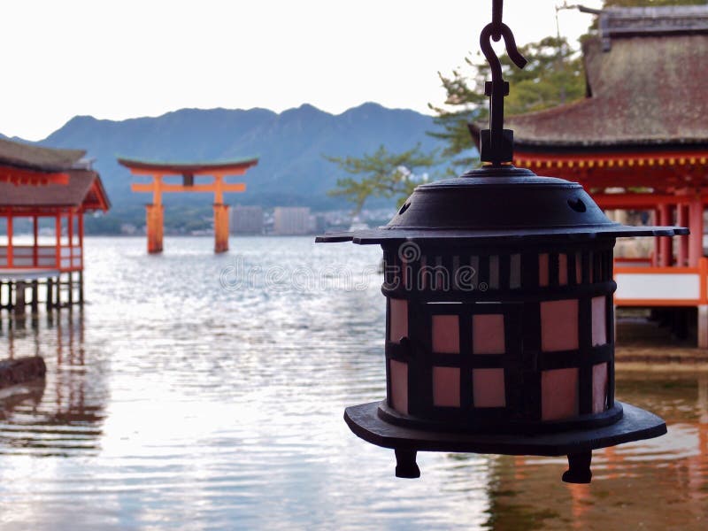 Miyajima, Hiroshima, Japan - October 29, 2018: Itsukushima Shrine. Floating torii gate is burred in the distance. Lantern is focused. Miyajima, Hiroshima, Japan - October 29, 2018: Itsukushima Shrine. Floating torii gate is burred in the distance. Lantern is focused