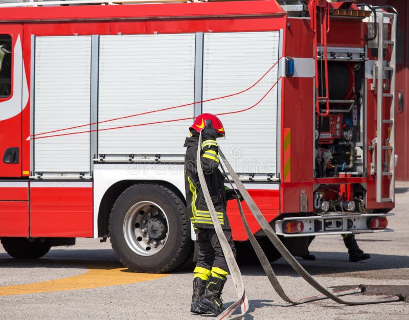 Sapadores-bombeiros com a mangueira para pôr para fora os fogos e o firetruc fotografia de stock royalty free Sapadores-bombeiros com a mangueira para pôr para fora os fogos e o firetruc fotografia de stock royalty free