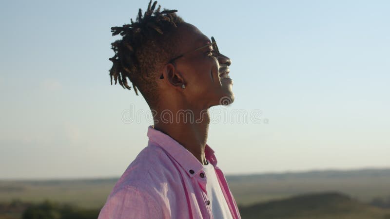 Satisfied african-american drinks cocktail, smiles and dances against the background of field. Happy man with black skin