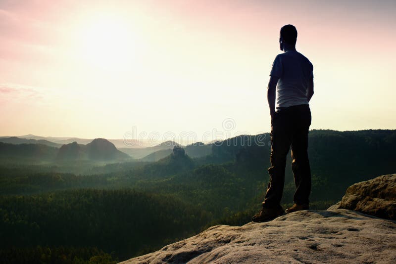 Satisfy hiker in grey shirt and dark trousers. Tall man on the peak of sandstone cliff watching down to landscape. Satisfy hiker in grey shirt and dark trousers. Tall man on the peak of sandstone cliff watching down to landscape.