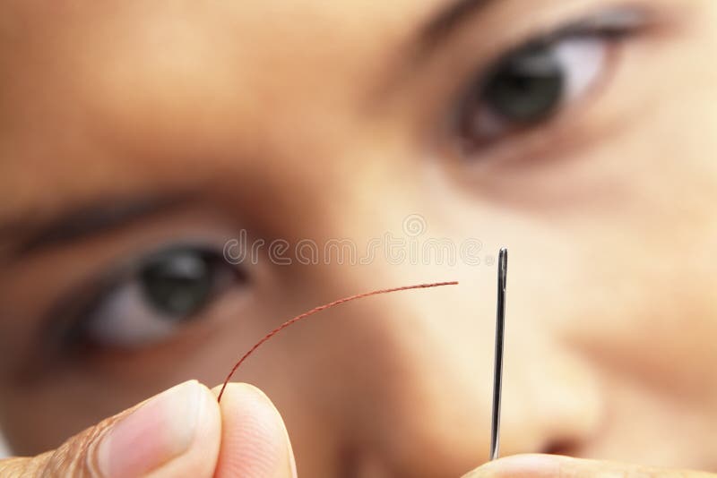 A young woman focus to put the sewing thread into needle. A young woman focus to put the sewing thread into needle