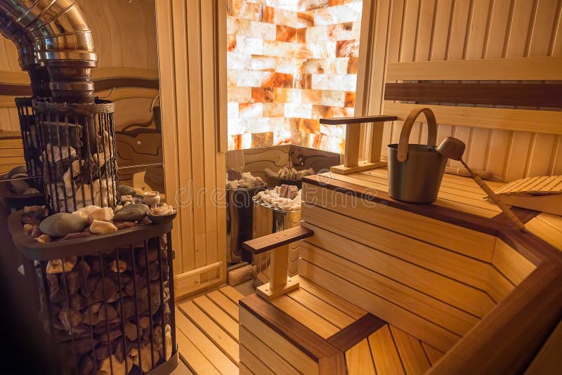 Sauna from wood. Stone wall with lighting from the inside. Classic accessories for bath. Ladle and bucket, stove with hot rocks