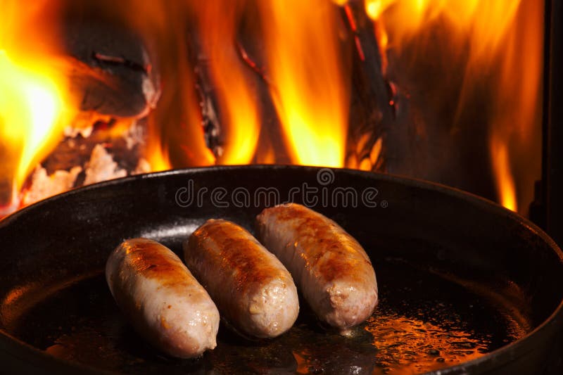 Sausage being fried in front of fire in frying pan. Frying pan stock images, royalty-free photos and pictures