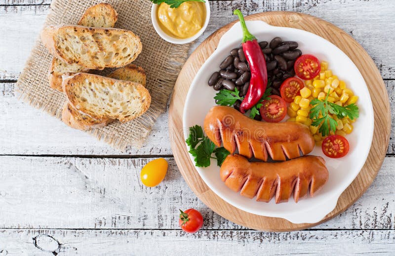 Sausages on the grill with vegetables on a platter. Top view