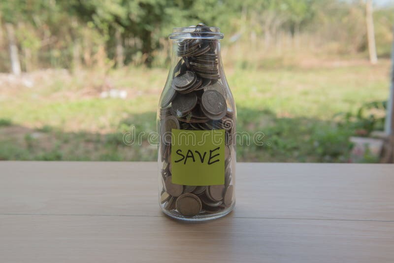 “Save†που γράφει στο έγγραφο, νομίσματα σε ένα βάζο γυαλιού στοκ φωτογραφία