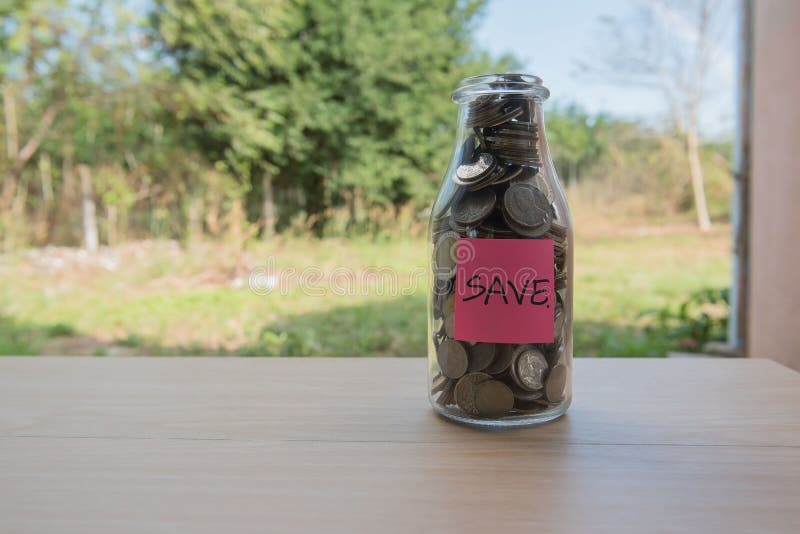 “Save†που γράφει στο έγγραφο, νομίσματα σε ένα βάζο γυαλιού στοκ φωτογραφία