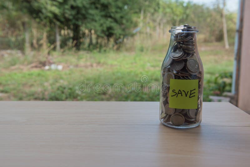 “Save†που γράφει στο έγγραφο, νομίσματα σε ένα βάζο γυαλιού στοκ φωτογραφία