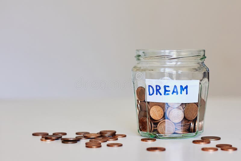 Saving money for dream concept. Glass jar full of coins and sign dream