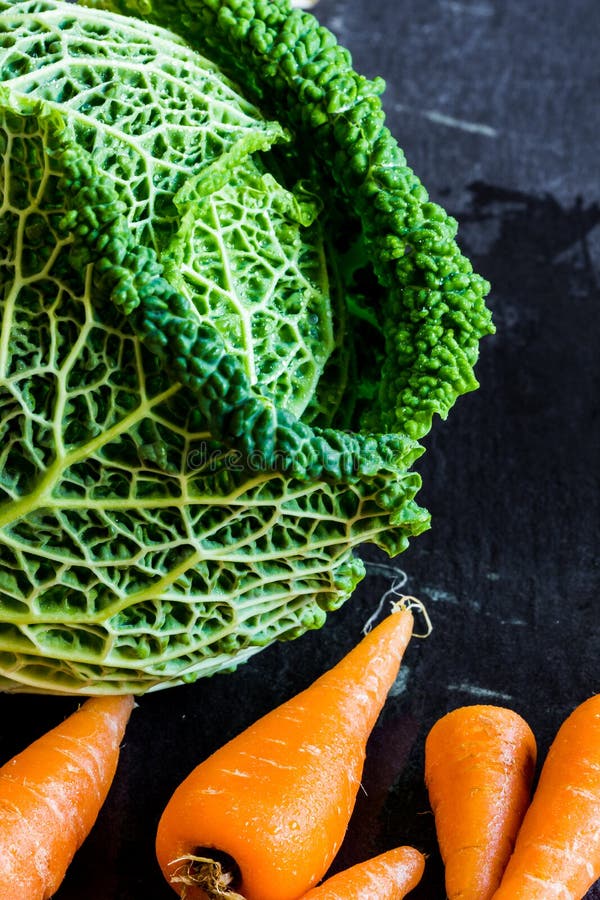 Fresh Savoy cabbage with baby chantenay carrots. Close up on slate background. Copy space, selective focus, vertical, macro. Fresh Savoy cabbage with baby chantenay carrots. Close up on slate background. Copy space, selective focus, vertical, macro