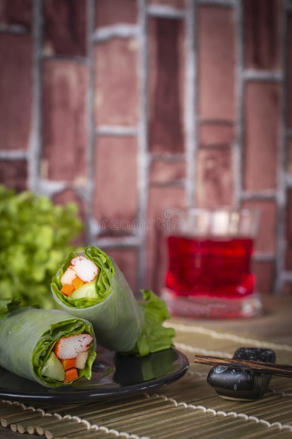 Sałatkowe rolki na czarnym talerzu umieszczającym na drewnianej arfie tam są chopsticks umieszczającymi obok i czerwonym wodą w s zdjęcie stock