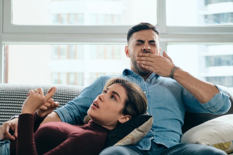 Bored men yawning while women keeps talking. Young couple having boring conversation at home. Bored men yawning while women keeps talking. Young couple having boring conversation at home.