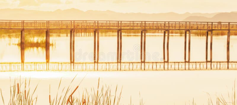 Sc?nique de la vue tropicale de lac au coucher du soleil, le pont en bois abstrait s'est refl?t? dans un lac, couvre de chaume l' photographie stock libre de droits Sc?nique de la vue tropicale de lac au coucher du soleil, le pont en bois abstrait s'est refl?t? dans un lac, couvre de chaume l' photographie stock libre de droits