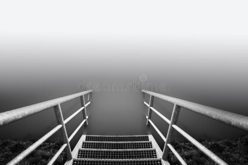 Scala di grigi scatto da una scala di scale giù verso un lago immagine stock