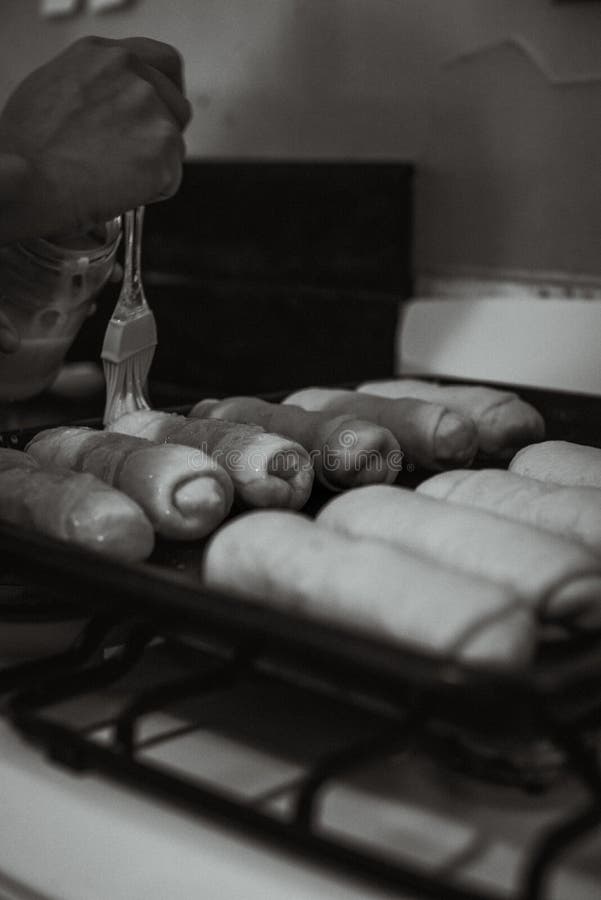 Scala di grigi verticale scattata su una panchina di spandimento dell'olio su panini di pane crudo con spazzola fotografia stock libera da diritti