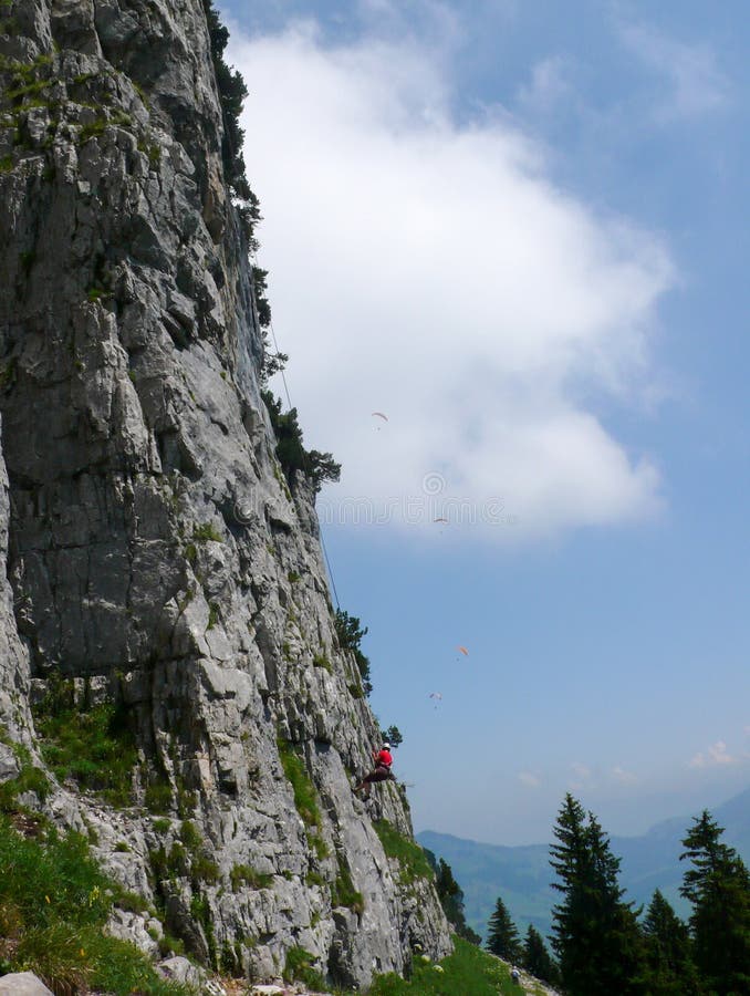 Scalatore che rappelling fuori da un fronte ripido della montagna della roccia su terra sicura con il volo dell'aliante nel cielo fotografia stock Scalatore che rappelling fuori da un fronte ripido della montagna della roccia su terra sicura con il volo dell'aliante nel cielo fotografia stock