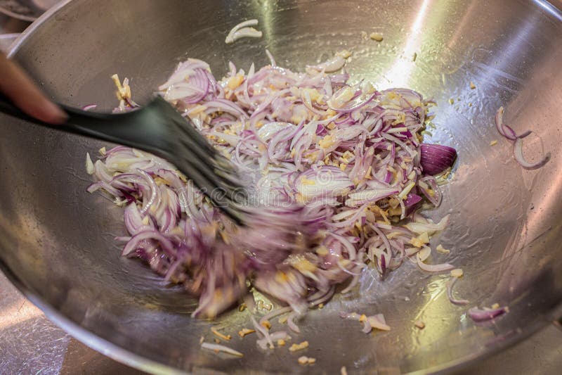 Stir-frying chopped onions,shallots and garlic in a stainless steel wok,or deep bottom round pan,with a black ladle. Stir-frying chopped onions,shallots and garlic in a stainless steel wok,or deep bottom round pan,with a black ladle.