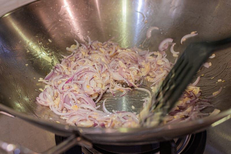 Stir-frying chopped onions,shallots and garlic in a stainless steel wok,or deep bottom round pan,with a black ladle. Stir-frying chopped onions,shallots and garlic in a stainless steel wok,or deep bottom round pan,with a black ladle.