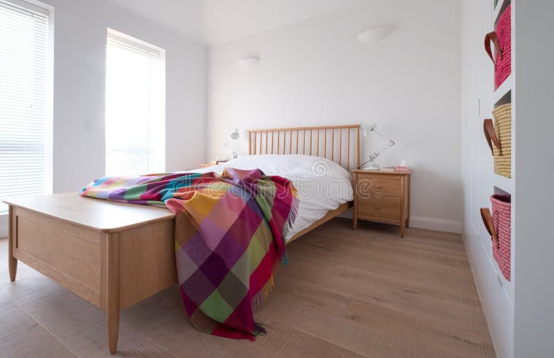 Scandi style bedroom interior with wooden bedroom furniture, white painted walls, white bedding and colourful blanket.