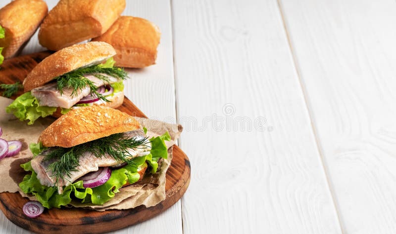 Scandinavian cuisine, seafood burger with freshly baked crispy bun, herring fillet, onions and lettuce. Dish served on a rustic