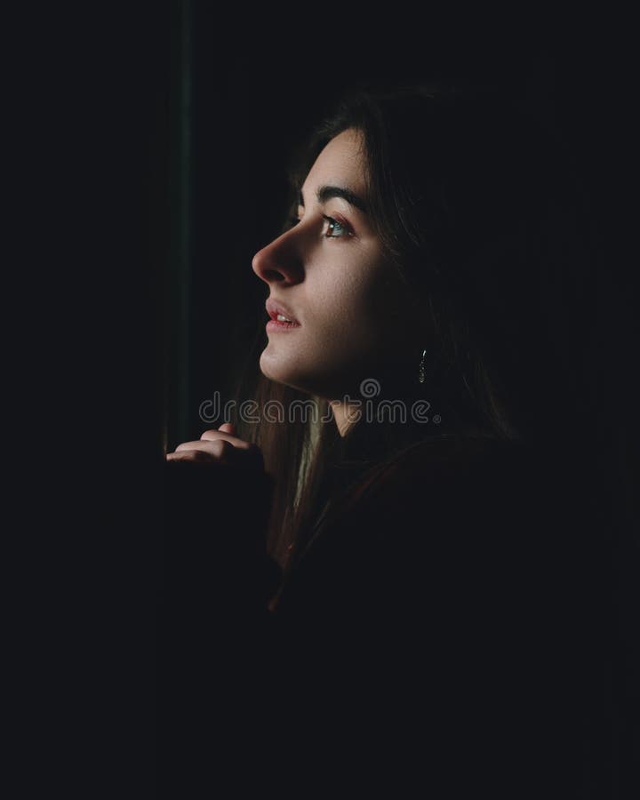 Scared beautiful woman profile looking up in dark. Sad teenager face depressed looking through a window in an abandoned house