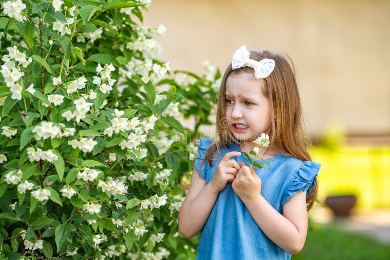 Scared little girl 4 years old near a Jasmine Bush, afraid of insects in the garden