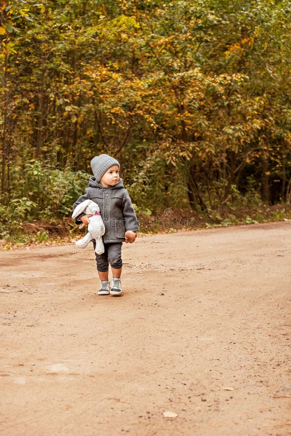 scared lost boy walking and looking people in the forest in a gray coat with a toy rabbit and mushroom in his hand